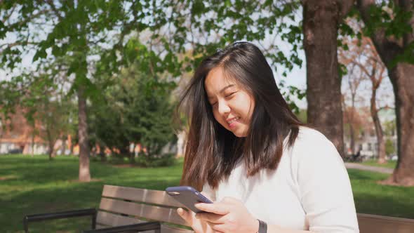 Close up face of Asian woman sitting on a chair at a park and using smartphone
