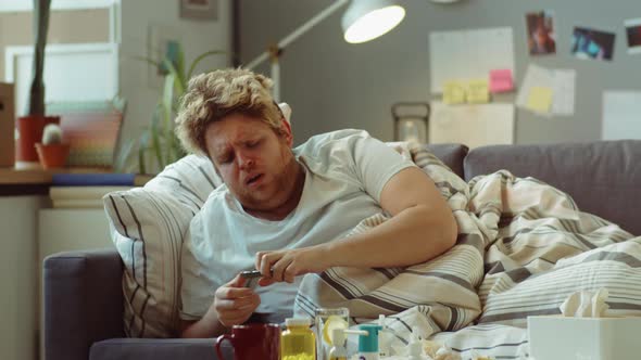 Sick Man Taking Pill while Lying on Sofa at Home