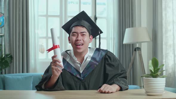 Excited Asian Man Showing Off A University Certificate During An Online Video Call At Home alt