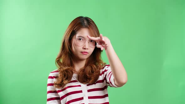 Young Asian woman with eyeglasses pointing to the eyes watching you gesture, keeping eyes on you, gr