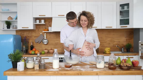 Pregnant Woman With Husband Cooking Together In Kitchen