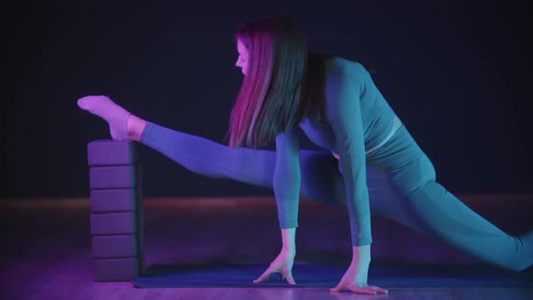 Young Woman Stretching Her Leg in Neon Lighting Putting Her Heel on the Special Stand and Stretching