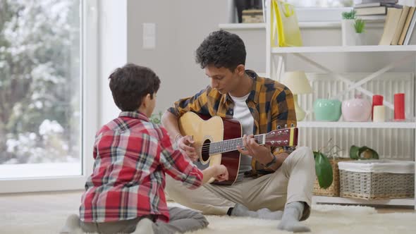 Wide Shot Portrait of Smiling Positive Middle Eastern Teenager Playing Song for Brother Distracting