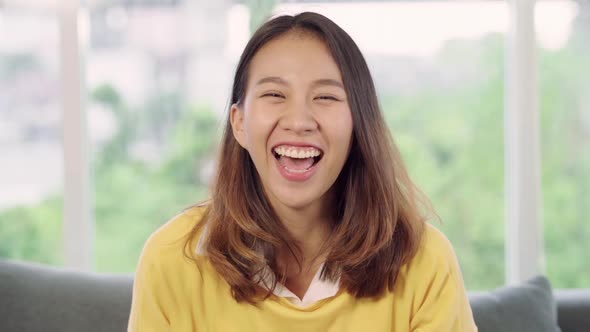 Asian woman feeling happy smiling and looking to camera while relax in her living room.