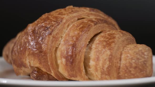 Croissant on white plate rotating in front of camera on black background