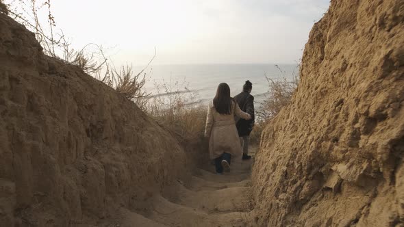 Happy Couple Goes Down the Stairs to the Wild Beach at Sunset