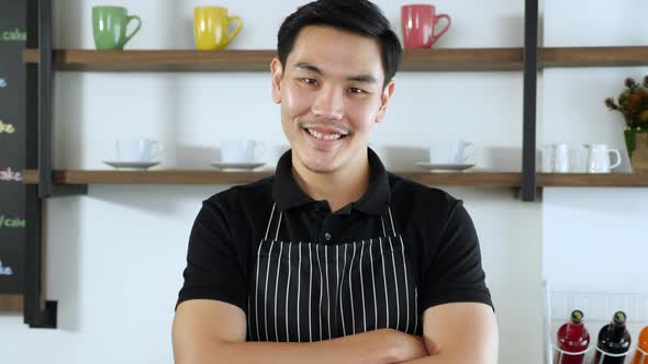 Portrait of Young asian male barista or waiter in polo shirt and apron smiling