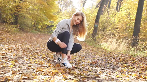 Sporty Blonde Tying Her Shoes for an Autumn Run in a Forest Park on a Sunny Beautiful Morning