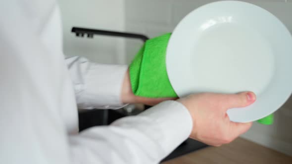 Caucasian man hands wipe wet dishes in the kitchen with a green towel. Close-up shot