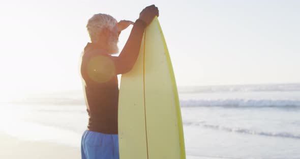 Senior african american man holding surfboard on sunny beach