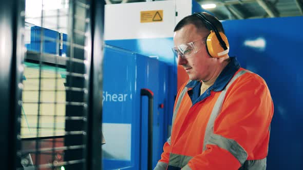 Male Engineer in Safety Wear is Operating an Industrial Machine