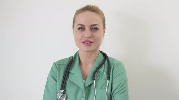 Smiling Female Doctor in Green Medical Coat with Arms Crossed Posing Looking at Camera Against White