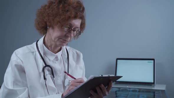 Concentrated Female Doctor Radinologist Writes Entries in Registration Book Works in Clinic Office