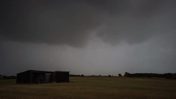 Stormy clouds moving in time lapse and raining over field with barn from different perspectives