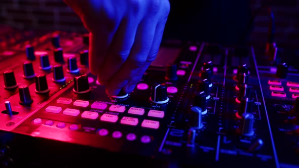 DJ twists knobs on mixing console behind his counter to set up rave in nightclub, closeup. DJ works