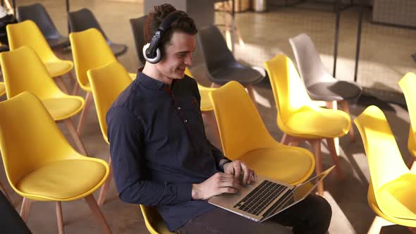 Young Attractive Guy is Dancing to Music in His Headphones While Working on Laptop
