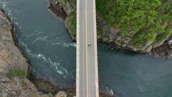 Top down drone view of a motorcycle passing over a bridge.