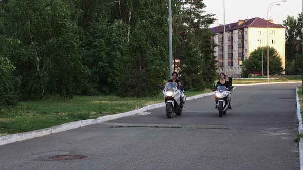 Two Young Women are Riding Motorcycles at Early Evening Without Helmets