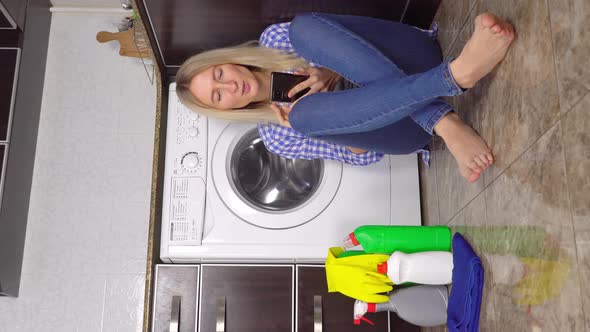 blonde in jeans and a shirt sits on the kitchen floor near the washing machine