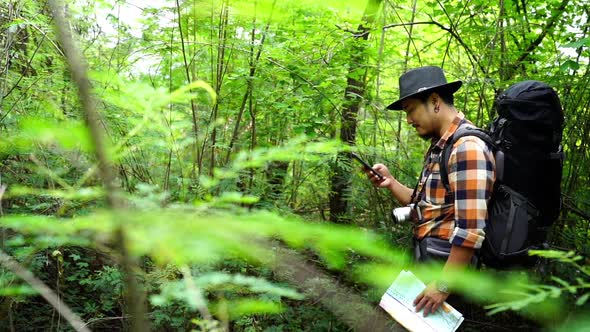 panning shot of man traveler with backpack using smartphone in the natural forest