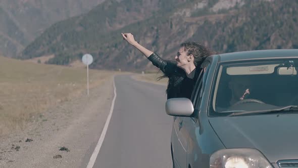 Young Girl Waves Hand and Enjoys Life Leaning Out of Car