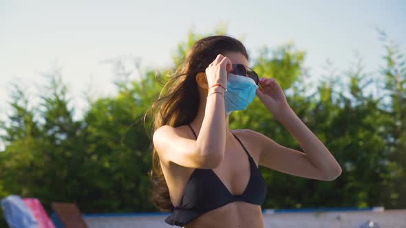Young Fit Woman Wearing Black Bikini Top and Face Mask Fixing Her Sunglasses
