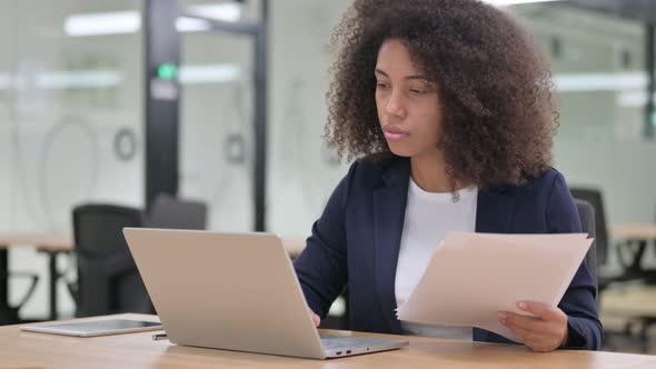 African Businesswoman with Laptop Reading Documents 