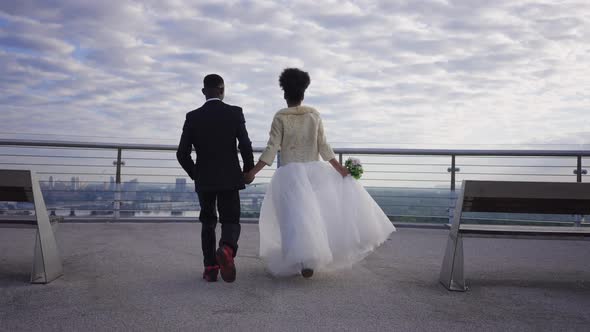 Excited African American Bride and Groom Running in Slow Motion to Bridge Handrails