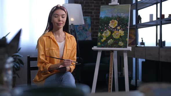 Attractive Asian Female Artist Sitting Near Canvas