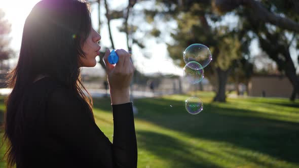 Beautiful young woman blowing bubbles floating in dreamy sunshine and lens flares outdoors at sunset