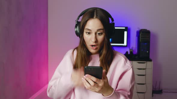 A Shocked Woman in Headphones is Looking to the Camera Siting Neon Light Background