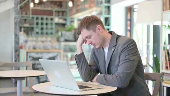 Young Man with Laptop Taking Nap in Cafe