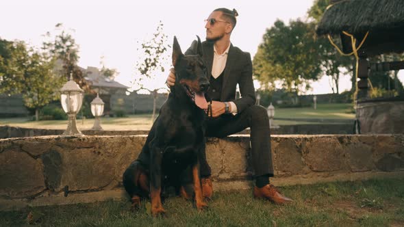 A Rich Businessman in a Business Suit Walks with a Big Doberman in the Park. A Successful Bearded