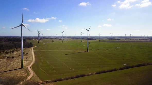Aerial view of wind turbines generating renewable energy in the wind farm, sunny spring day, low fly