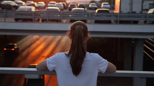 Young Schoolgirl with Ponytail Looks at Sunset on Bridge