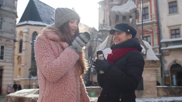 Two Smiling Women Tourists Traveling Together Drinking Hot Tea Coffee From Thermos on City Street