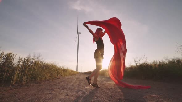 Woman with Pieces of Red Cloth Dance Near the Field with Wind Generators 