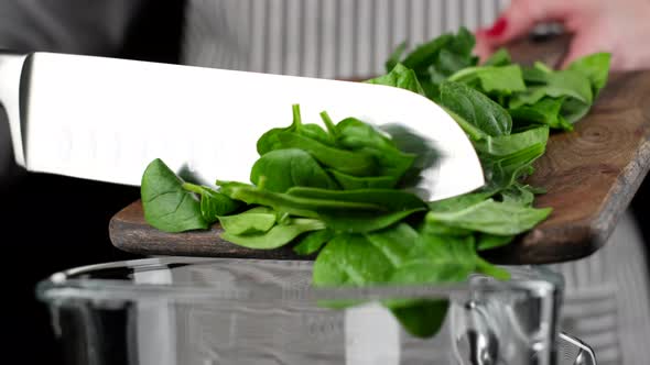 The chef pours chopped spinach from cutting wooden board to blender