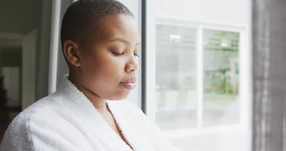 Thoughtful african american plus size woman wearing robe, looking through window