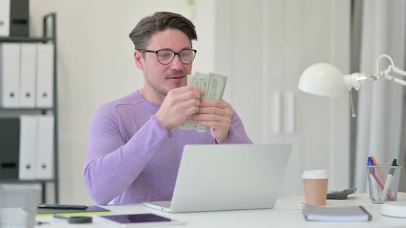 Middle Aged Man with Laptop Counting Dollar in Office 