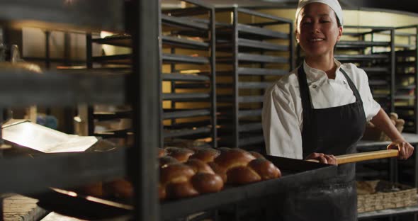 Animation of happy asian female baker holding wooden spatula with challah