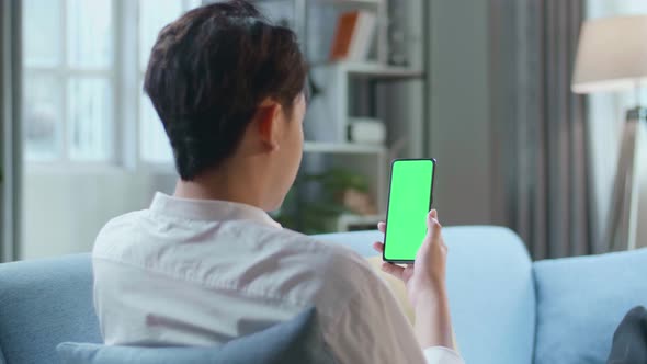 Man Watching Smartphone With Green Screen While Lying On Sofa In The Living Room