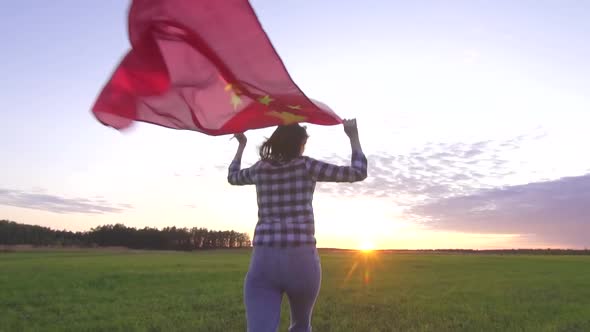 Young Positive Woman Runs Across the Field at Sunset with the Flag of China Slow Mo