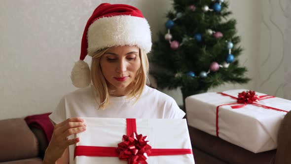 Adorable woman in Santa Claus hat opening her Christmas gift box