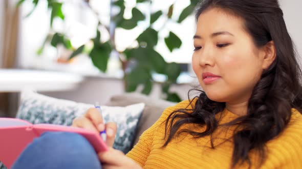 Asian Woman with Diary Sitting on Sofa at Home