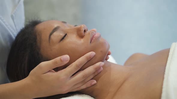 Multi Ethnic Calm Young Woman Is Getting Medical Face Massage From Professional Hand