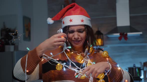 Festive Woman with Santa Hat Trying to Untangle Lights