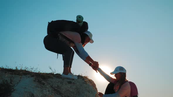 Girl Helps Her Friend Climb Up the Last Section of Mountain. Tourists with Backpacks Help Each Other