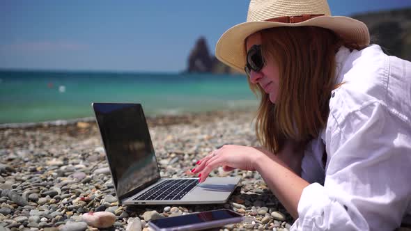 Successful Business Woman in Yellow Hat Working on Laptop By the Sea
