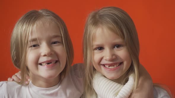 Two Little Toothless Girls are Smiling Against an Orange Background